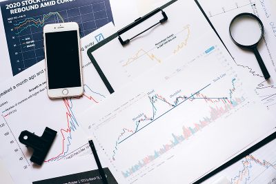 Lupe, Handy und Blätter mit Graphen und Analysekurven auf Klemmbrettern von oben Lupe, Handy und Blätter mit Graphen und Analysekurven auf Klemmbrettern von oben