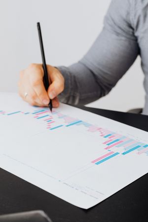 Eine Person zeigt mit einem blauen Stift auf ein Balkendiagramm in einem Dokument.