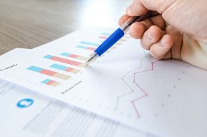 Eine Person markiert mit einem Stift Daten auf einem Diagramm. Fokus auf Analyse und Planung.