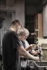 Junger Mann neben älterem Mann in einer Werkstatt bei der Ausbildung vor einer Werkbank