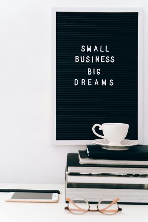 Schwarzes Schild mit Aufschrift „Small Business Big Dreams“. Darauf eine Tasse und Bücher.